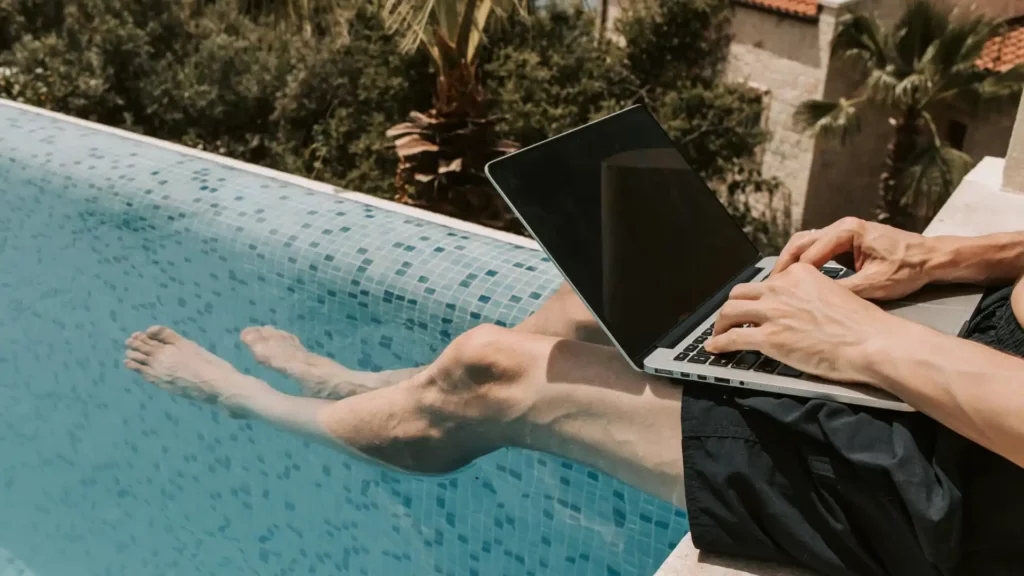 Um jovem com seu notebook na beira da piscina enquanto trabalha.